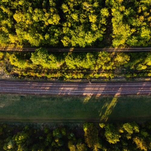 Aerial shot of rail tracks surrounded by forests under the sunlight in Germany Capacitación Técnica–Práctica: Gestión Ambiental Aplicada a la Construcción de Carreteras y Vías Férreas